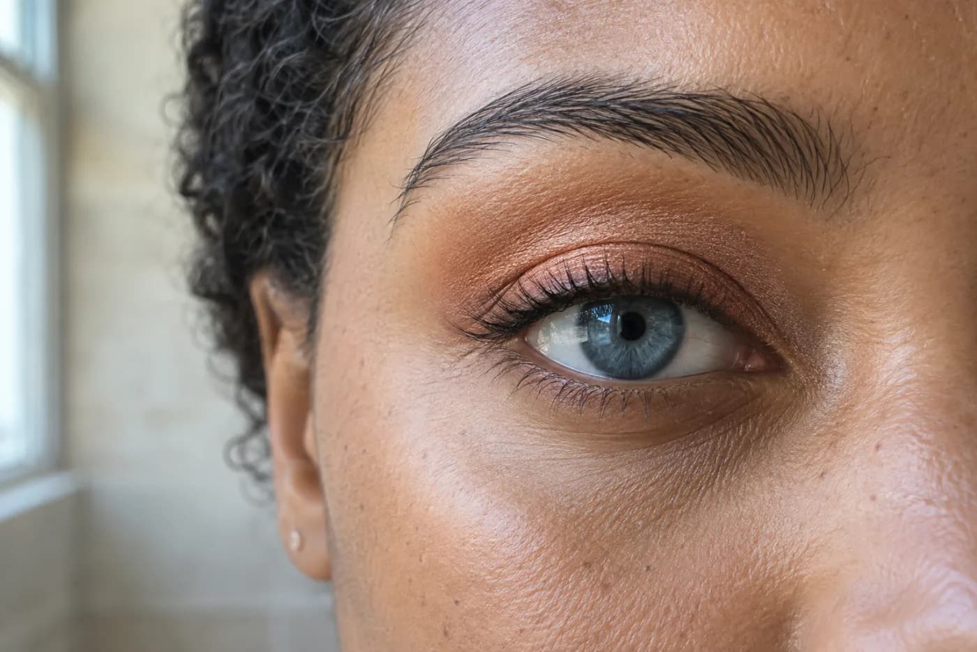 Close detail of a blue eye framed by a thin muted copper satin eyeshadow wash and a natural brow in daylight
