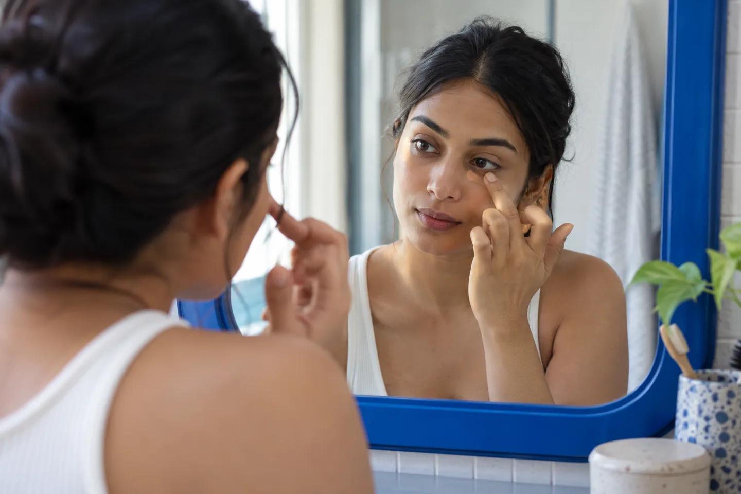 Young woman tapping a small amount of peach corrector at the inner under-eye area