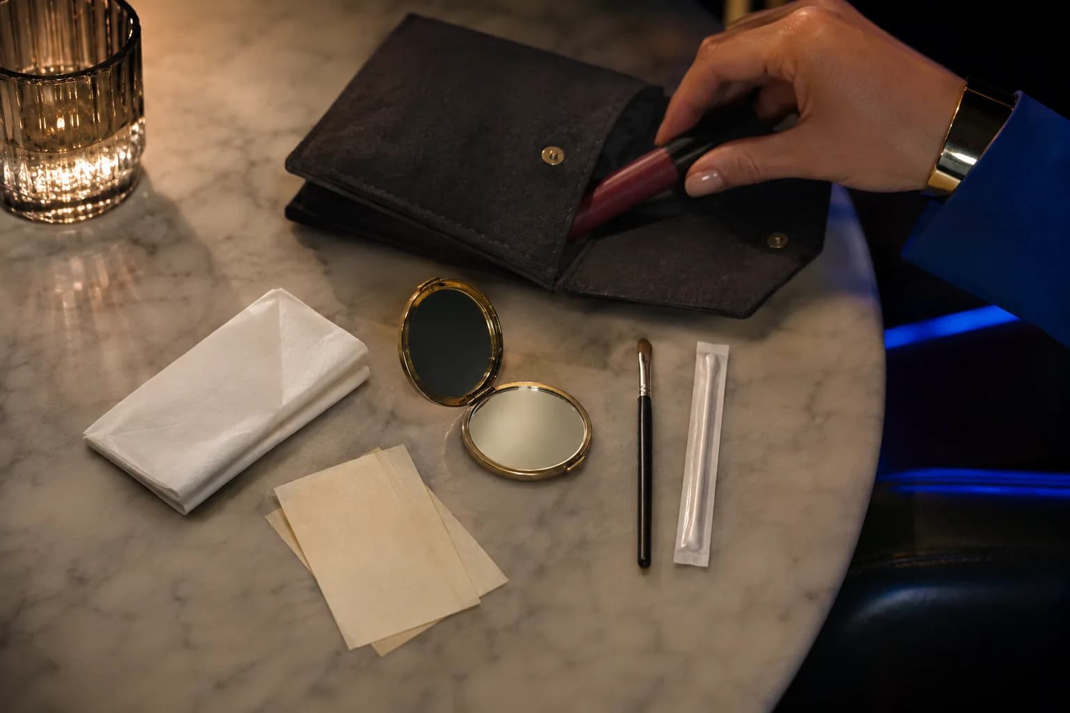 Neceser pequeño sin marcas con papel absorbente, color baya, espejo y bastoncillo sobre una mesa de café