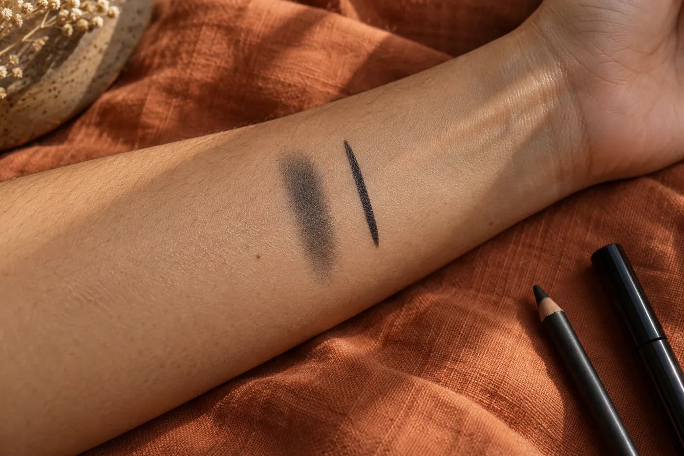 Trace anthracite douce et ligne étroite nette sur un avant-bras olive posé sur du lin rouille près de produits sans marque