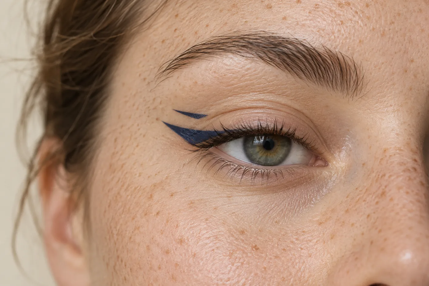 Close view of a freckled adult's open eye with a navy outer wing and a separate short upper stroke leaving visible skin between