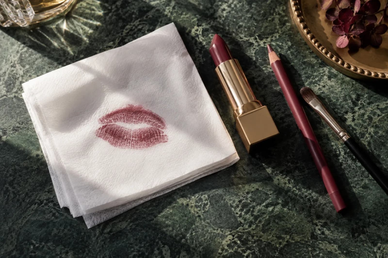 Gedempte berryafdruk op een gevouwen tissue naast merkloze lipstick, potlood en zacht kwastje