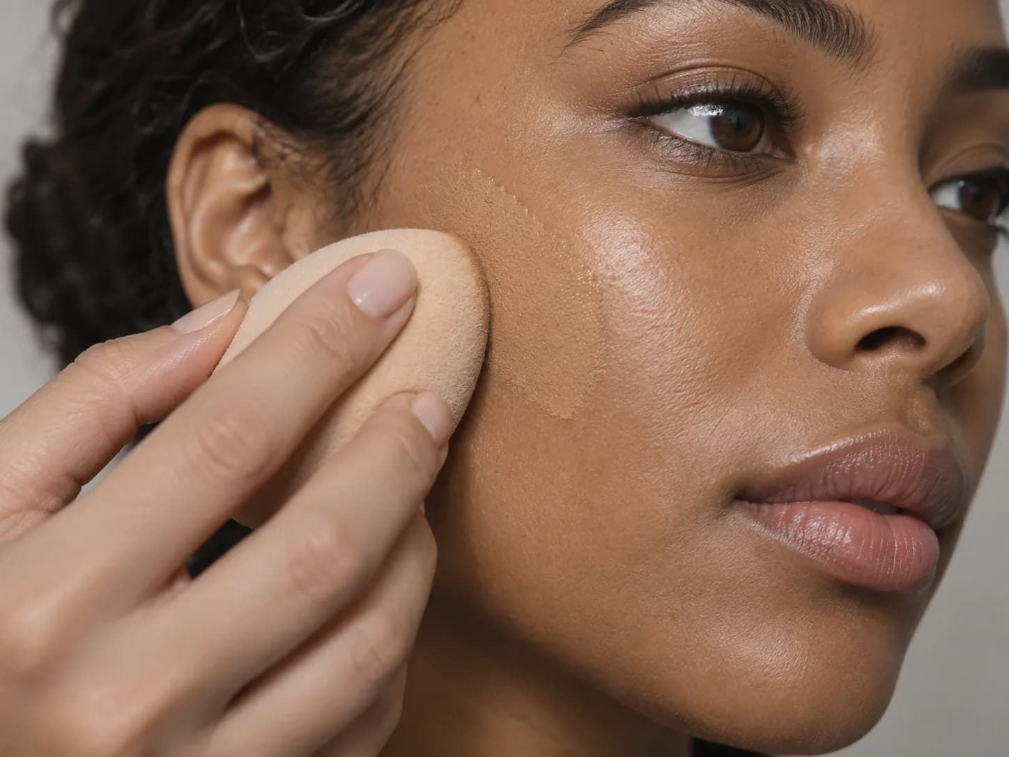 Saubere Finger drücken einen Makeup-Schwamm über eine dünne Foundation-Schicht auf mittelbrauner Haut