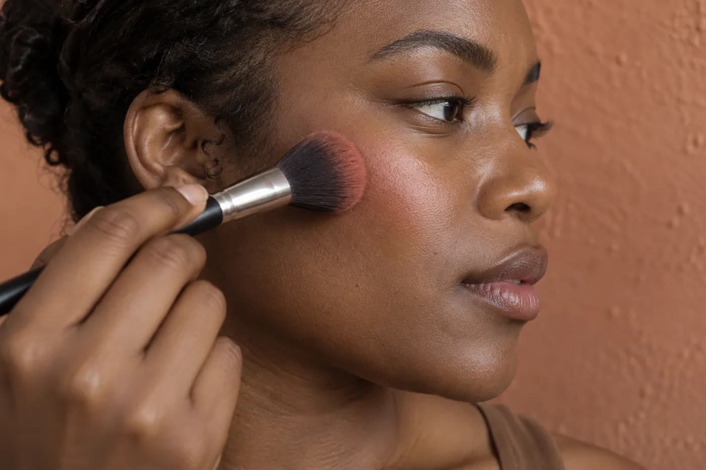 Pincel macio e limpo aplica uma camada fina de blush coral em uma bochecha de pele negra